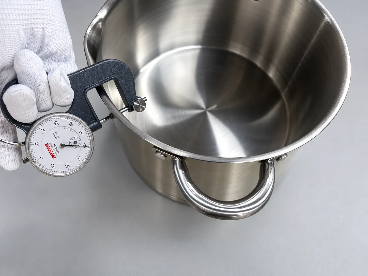 Measuring the wall thickness of a stainless steel pot with a dial thickness gauge
