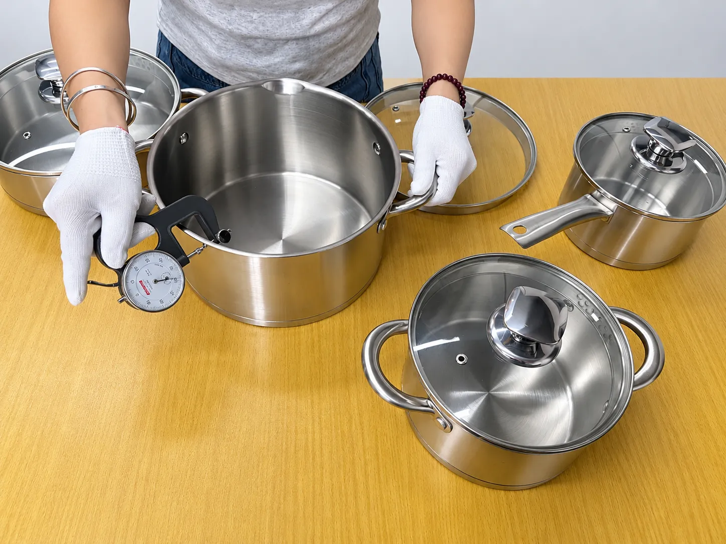 Gloved inspector checking a stainless steel cookware wall with a thickness gauge